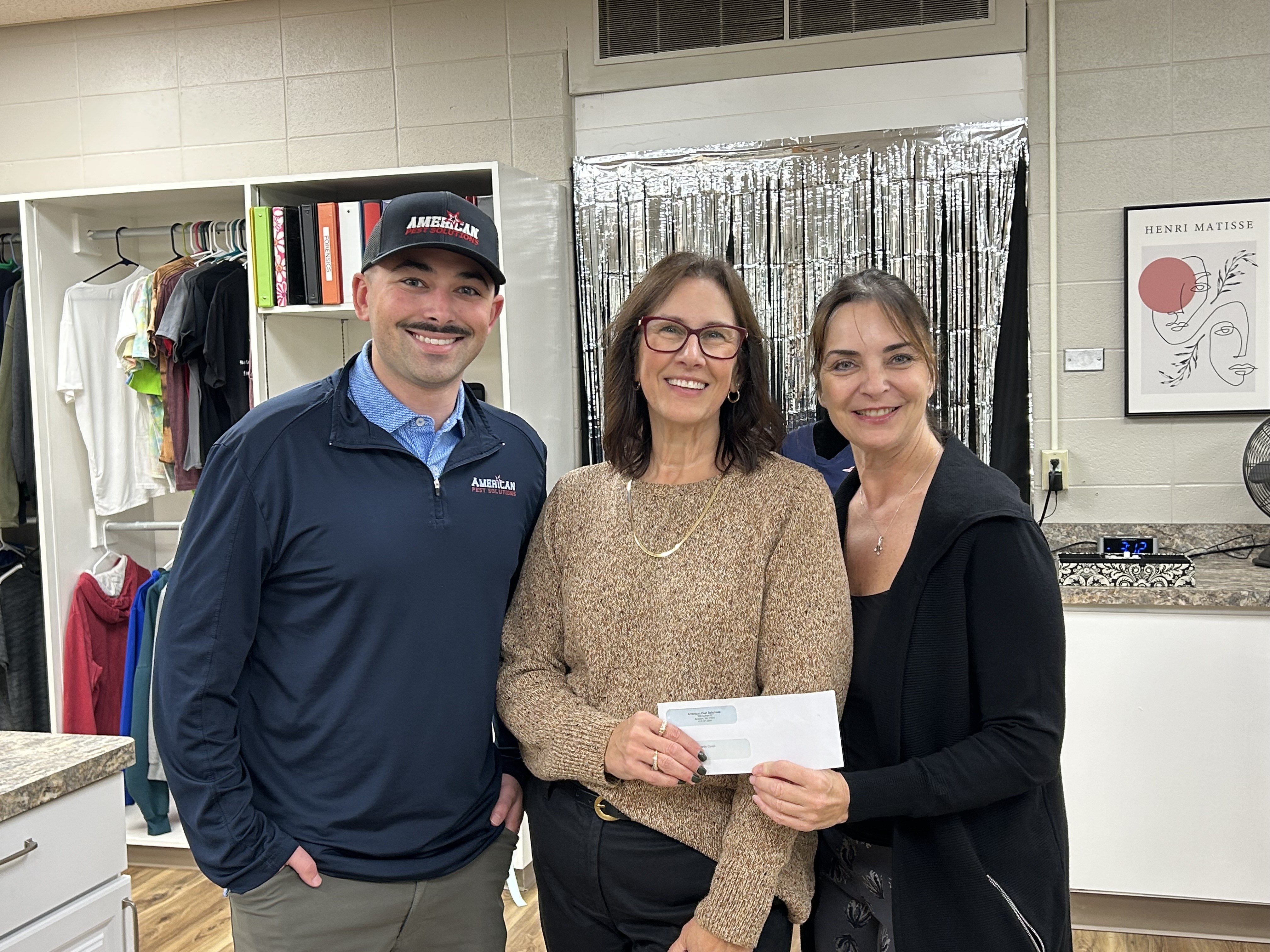 Jill Keenan holds an envelope with an American Pest Solutions employee and another woman after receiving a donation.