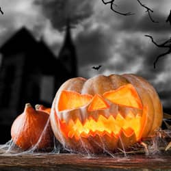 An image of a lit-up Halloween-carved pumpkin on the ground with webs and a dark sky background